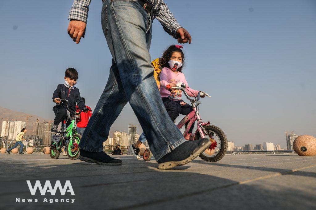 Iranian children, using face masks after recording the statistics of coronavirus in Iran exceeded 5,500 daily cases and more than 300 deaths a day, riding their bikes in a promenade called Chitgar Lake, (COVID19), in the west of Tehran, Iran October 23, 2020. Picture taken October 23, 2020. Majid Asgaripour/WANA (West Asia News Agency)