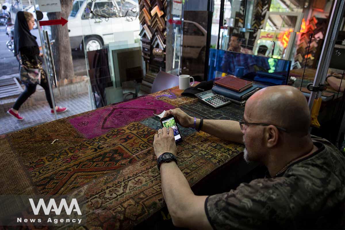 A glass seller in his shop checking election news via smartphone / WANA News Agency