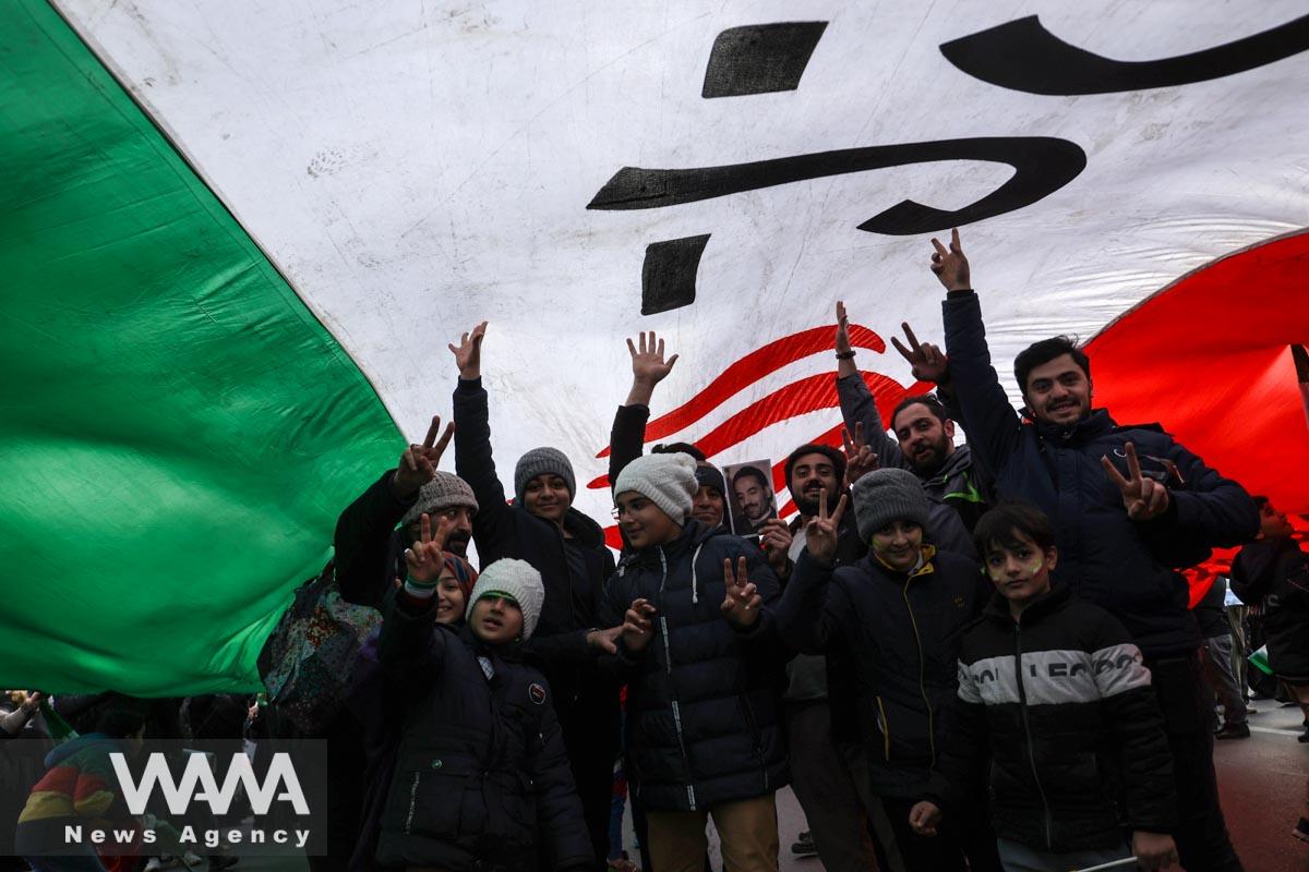 Iranians are seen under a large flag of Iran during the 44th anniversary of the Islamic Revolution in Tehran, Iran, February 11, 2023. Majid Asgaripour/WANA (West Asia News Agency)