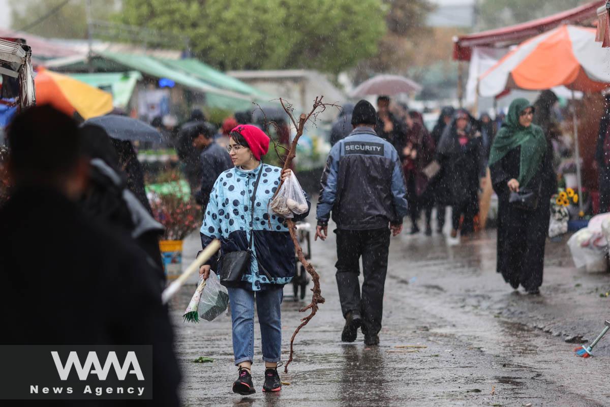 An Iranian woman walks through rain in a flower market, ahead of Nowruz, the Iranian New Year, in Tehran, Iran March 16, 2023. Majid Asgaripour/WANA (West Asia News Agency)