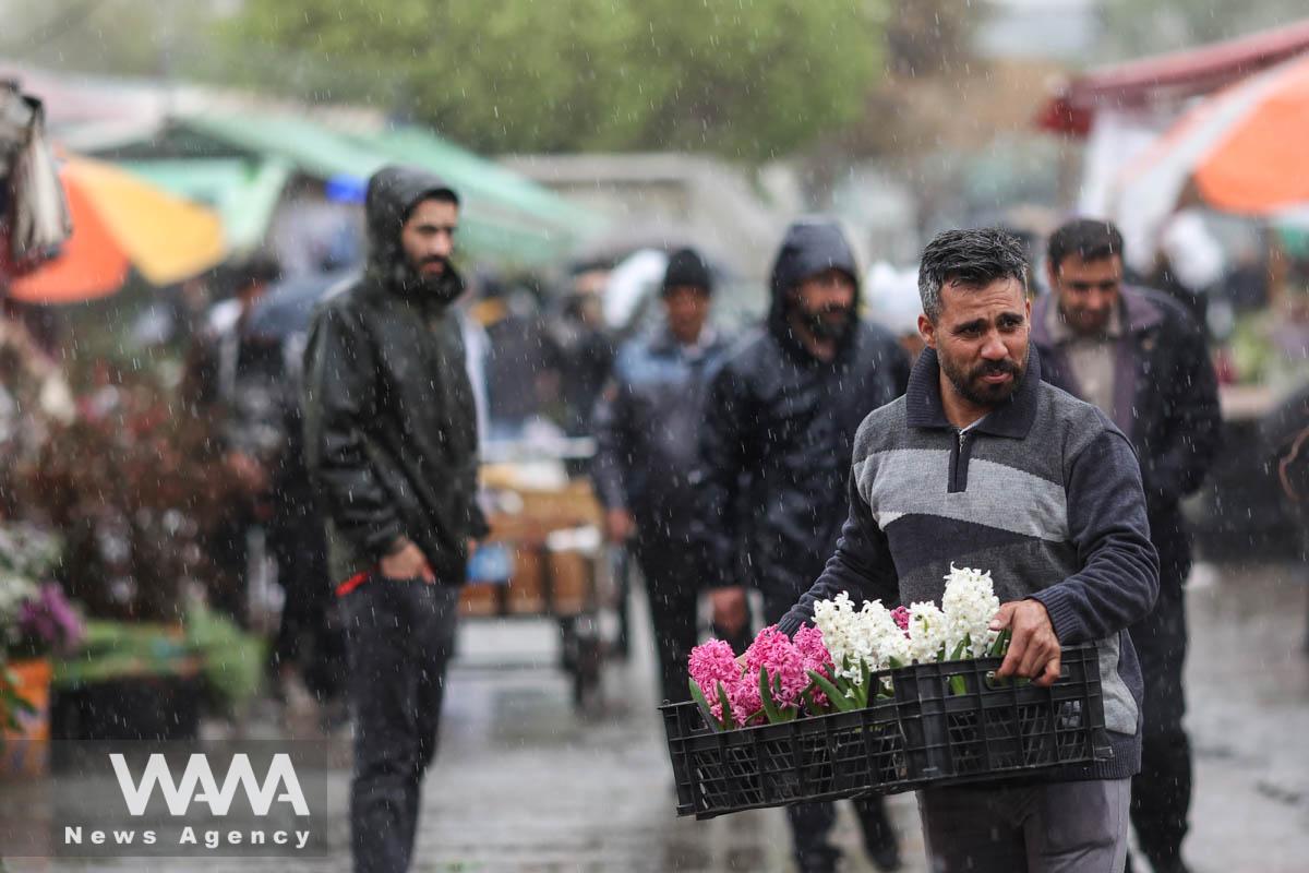 An Iranian man holds flowers through rain in a flower market, ahead of Nowruz, the Iranian New Year, in Tehran, Iran March 16, 2023. Majid Asgaripour/WANA (West Asia News Agency)