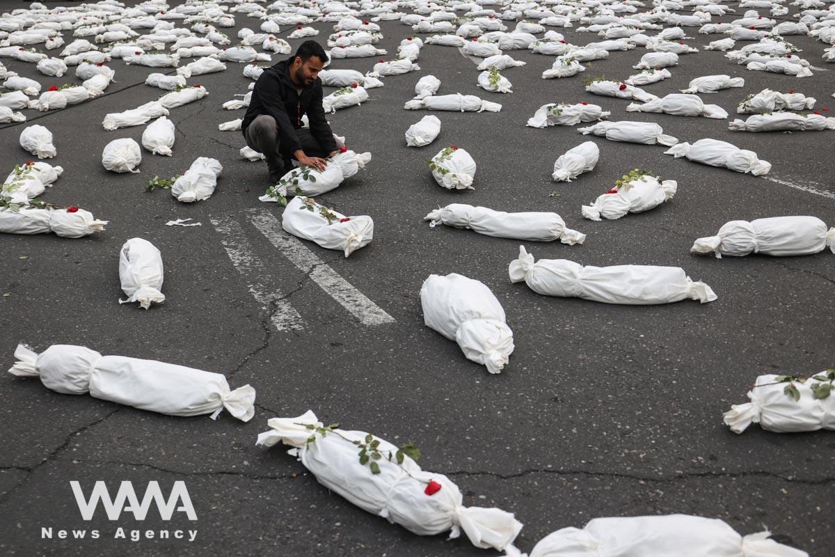 An Iranian man sits next to the Symbolic shrouds of Gaza children's dead bodies during a gesture in a street in Tehran/WANA (West Asia News Agency)
