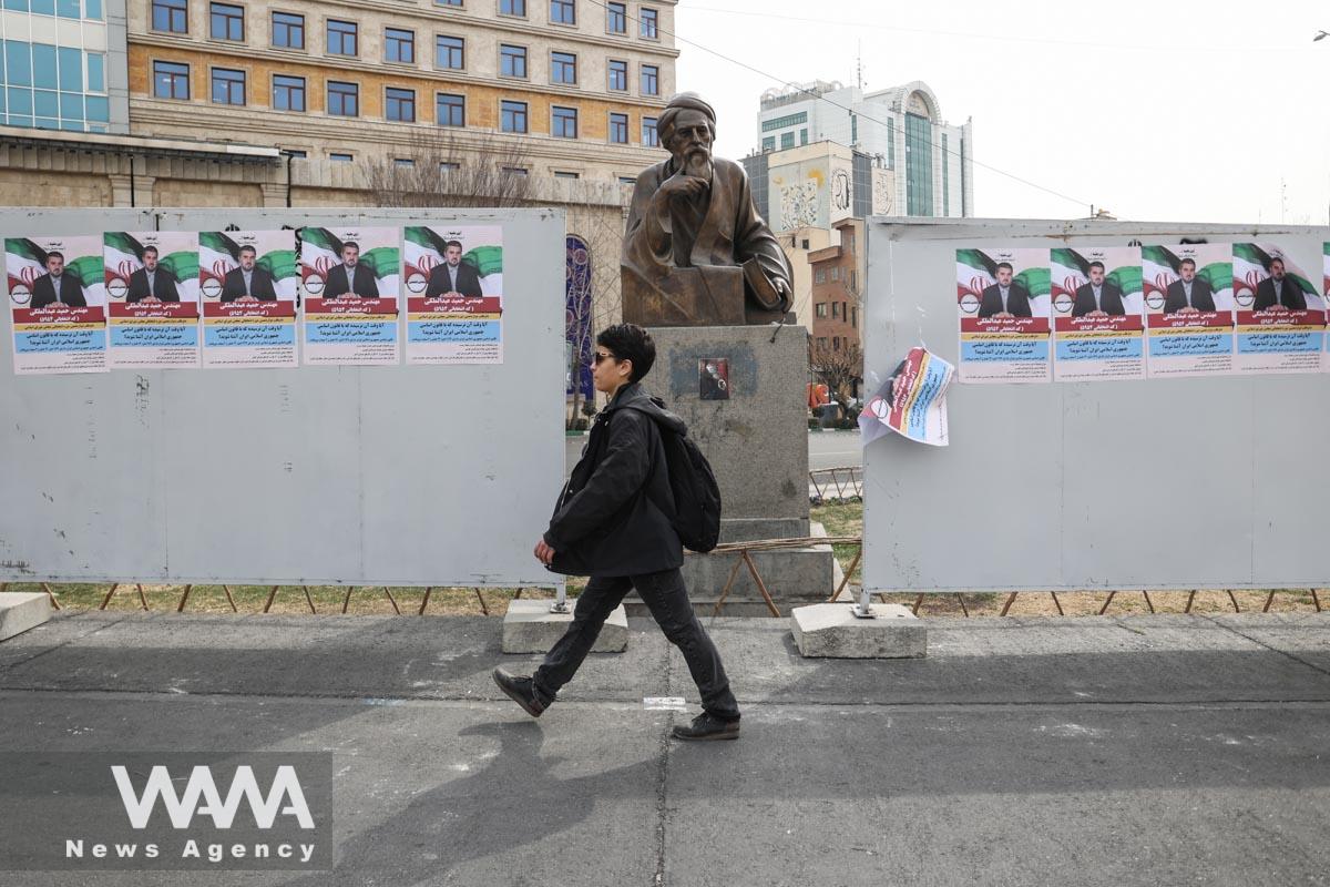 An Iranian man walks past campaign posters for the parliamentary election