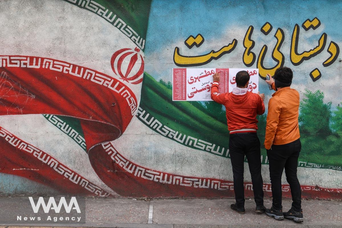 Iranian men put campaign posters on a wall during the last day of election campaigning