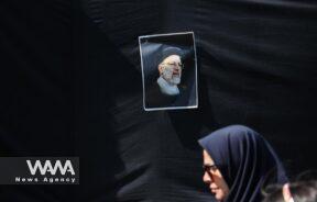 People walk near a banner with a picture of the late Iran's President Ebrahim Raisi on a street