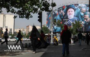 People walk near a banner with a picture of the late Iran's President Ebrahim Raisi on a street