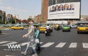 People walk past a billboard with a picture of the presidential candidates on a street