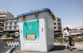 A man walks past a symbolic ballot box for the presidential election in a street in Tehran