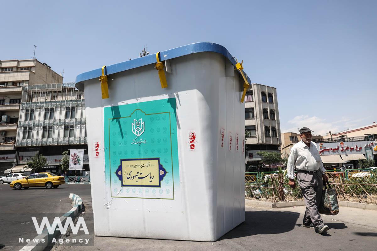 A man walks past a symbolic ballot box for the presidential election in a street in Tehran