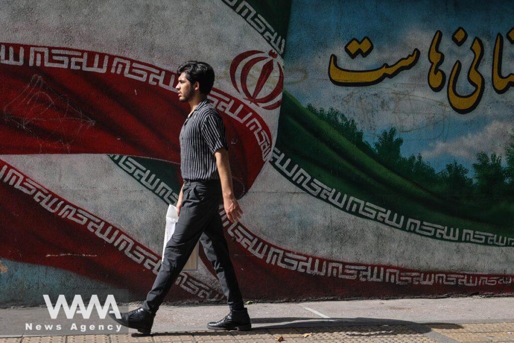 An Iranian man passes in front of a mural with the Iranian flag on a street in Tehran