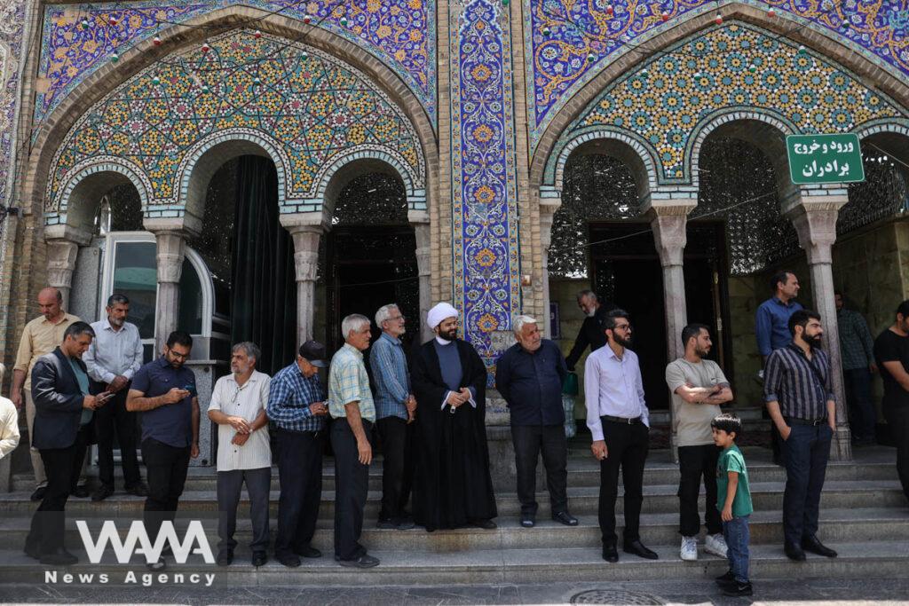 Iranian people stand in a queue as they wait to vote at a polling station in a snap presidential election to choose a successor to Ebrahim Raisi following his death in a helicopter crash