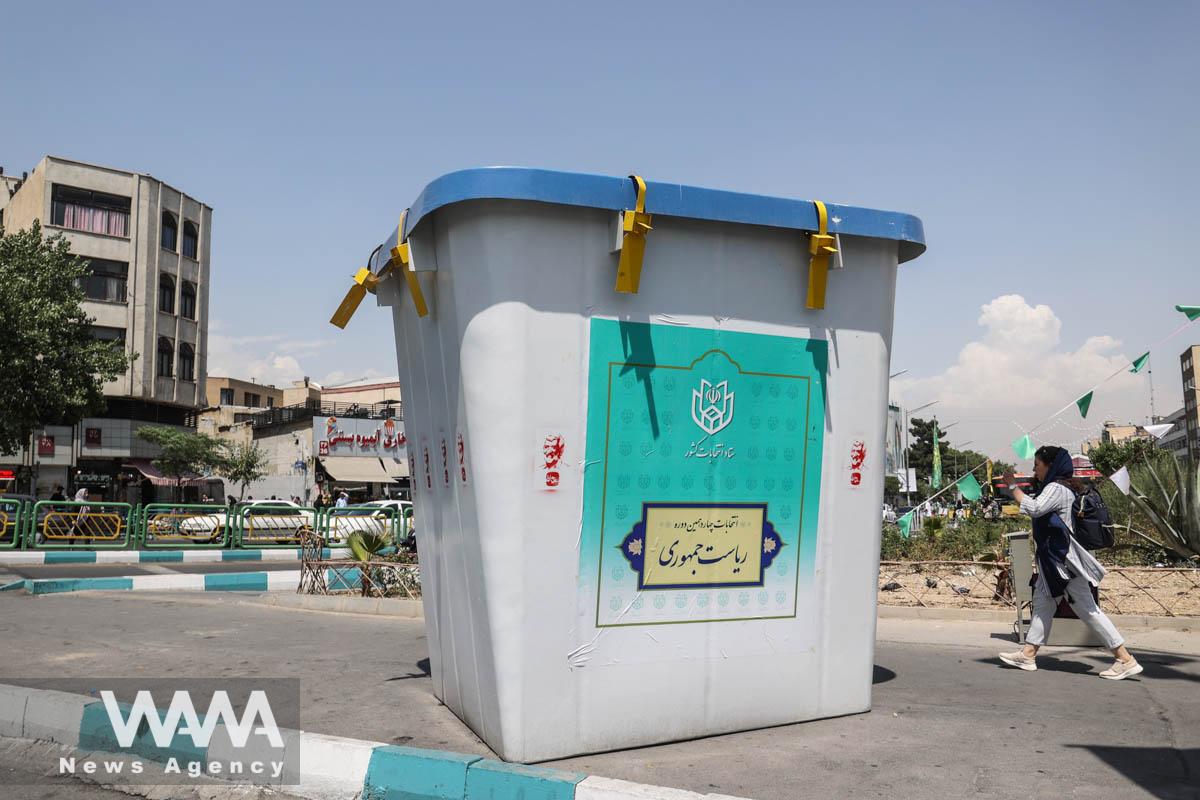 A woman walks past a symbolic ballot box for the presidential election in a street in Tehran