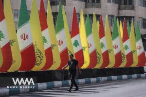 An Iranian man walks next to the stands with the flags of Iran, Hezbollah and Lebanon in a street